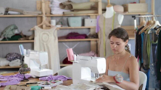 Female clothing designer stitching fabric on sewing machine in studio 