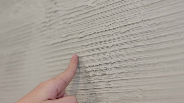 Close Up of Hand Touching Textured Grey Plaster Wall Surface