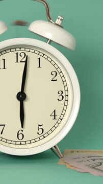 A charming white alarm clock rings vibrantly on a serene teal surface. Its classic bells furiously strike, marking the precise hour of 6 o'clock. A crisp morning awakening unfolds.