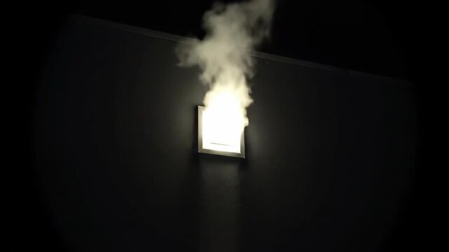 Smoke billows from a bright vent on a dark wall at night creating a mysterious and ominous mood