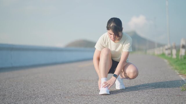 Young adult woman suffering from acute ankle pain during running workout. Female runner holding her leg due to sports injuries, ankle sprains or achilles tendonitis. Medical and healthcare concept