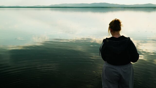 A female fisherman is fishing on a lake, surrounded by a swarm of blood-sucking mosquitoes that are causing her discomfort. Real footage with no staged elements.