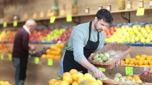 While working in shop, employee forms display case, puts ripe pears in pile. High quality 4k footage