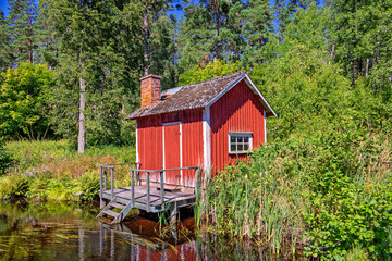 Red cottage with a jetty at a forest lake a beautiful sunny summer day © Lars Johansson