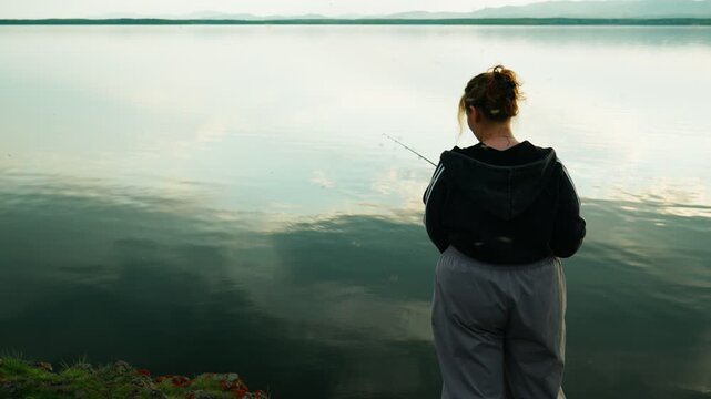 A female fisherman is fishing on a lake, surrounded by a swarm of blood-sucking mosquitoes that are causing her discomfort. Real footage with no staged elements.