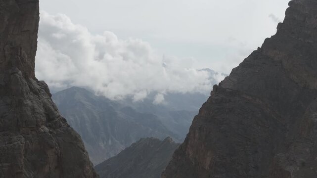 Stunning drone footage flying between two mountain ridges and emerging to reveal a breathtaking panorama of layered Himalayan peaks with beautiful clouds floating above the majestic landscape