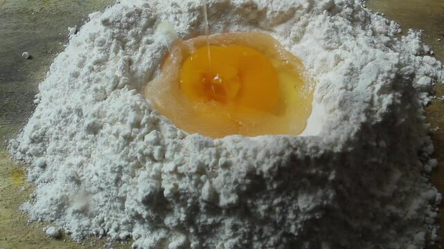 a close up of cracking an egg into flour on a wooden table