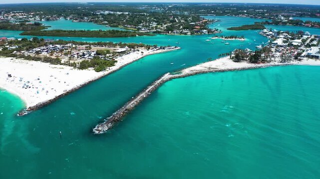 A jetty extends into aquamarine waters, separating sandy beaches from inland waterways. Perfect for travel content or coastal development features.