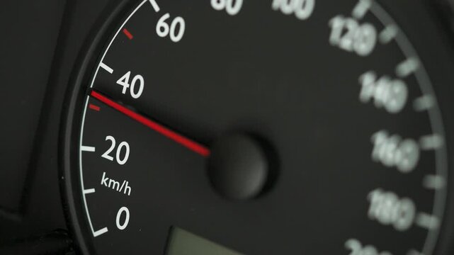 Close-up of a car speedometer showing approximately 30 kmh with a red needle and blurred blue police lights in the background. Concept image for speed control, traffic enforcement, urban driving