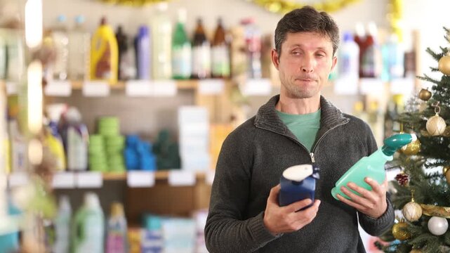 Man chooses spray glass cleaner in a supermarket before Christmas. High quality 4k footage