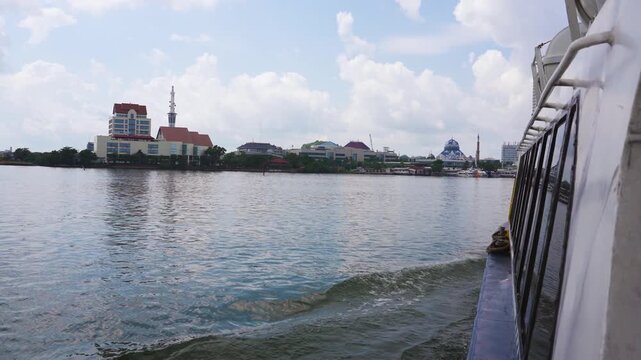 BATAM, INDONESIA - NOVEMBER 01, 2025: View of the Great Jami' Mosque and city skyline from the side of a moving ferry. Modern waterfront architecture under a cloudy sky.