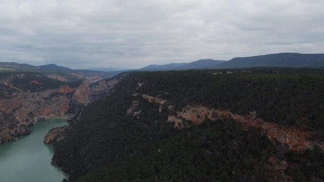 Spectacular 4K aerial drone view flying over the massive Jucar River canyon and reservoir in Castilla-La Mancha, Spain. See sheer rock cliffs dropping into turquoise water with dense, lush forests on