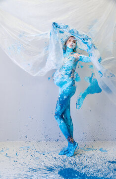 Pregnant woman covered in vivid blue body paint holding translucent fabric expressive contemporary maternity artwork blending movement color texture and emotion