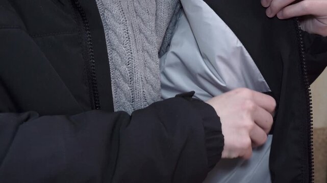 Demonstration of the inner pocket and lining of a winter jacket, A close-up of a person showing the inner pocket of a black jacket, Hand unbuttoning or checking the capacity of the zipper/velcro pocke