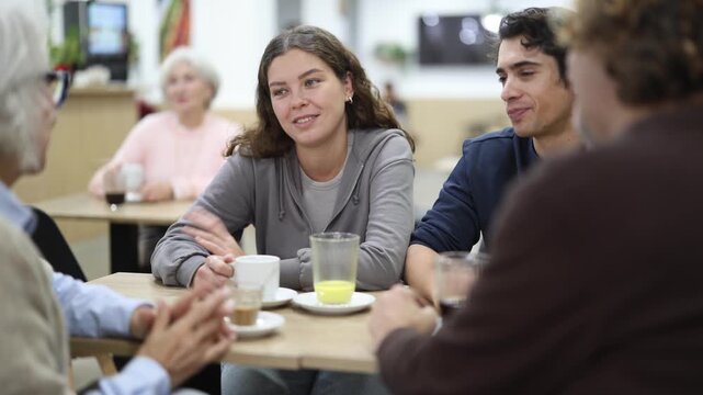 Family consisting of different generations sits at a large table in a cafe and discusses joint plans and holidays. Grandchildren communicate with their grandmothers in a coffee shop
