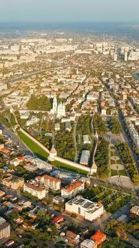 Vertical video. Astrakhan, Russia. The Astrakhan Kremlin, its white stone walls and emerald-domed Assumption Cathedral rising above the Volga River, aerial panoramic view under bright summer sky. Dro