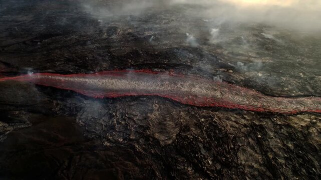 Aerial view of a long river of glowing lava across a basalt field