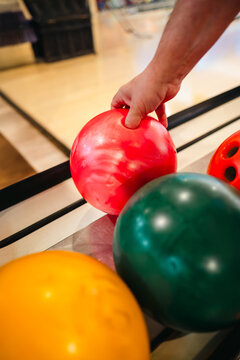 Man's hand at bowling holding red ball in indoor alley
