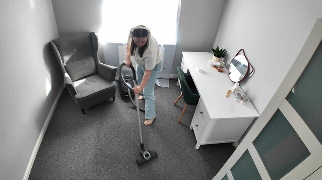 Woman dancing while vacuum cleaning and listening to music at home