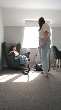 Mother vacuum cleaning while talking with daughter reading book