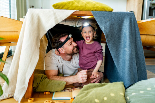 Dad and child building and playing in cozy blanket fort.