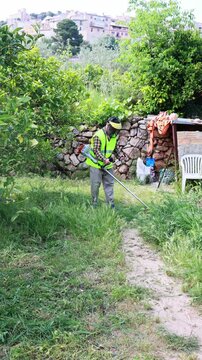 Gardener trimming overgrown grass with a string trimmer