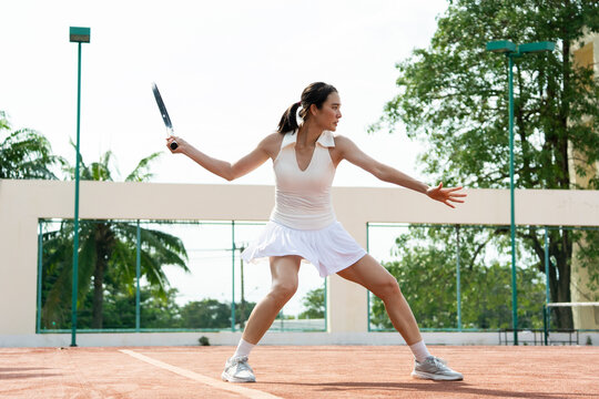 Asian young sportswoman exercise, playing tennis on outdoor clay court. 