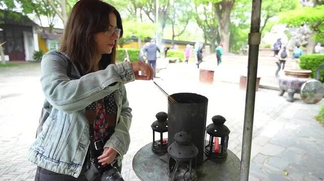 Woman performing a religious offering by burning incense sticks in a Buddhist temple in Suzhou