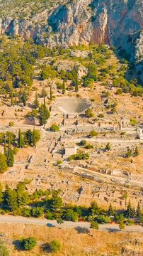 Vertical video. Delphi, Greece. Ruins of the ancient city of Delphi, stone foundations and columns scattered across the sacred slopes of Mount Parnassus, Drone footage under bright summer morning sun