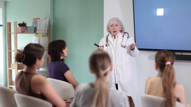 Senior woman doctor speaks to audience of listeners, carry out lecture. Female students are sitting in study room, listening to lecture, first aid help course