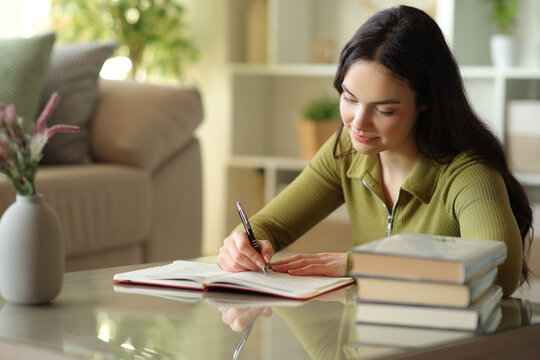 Serious young woman writing notes in paper agenda at home