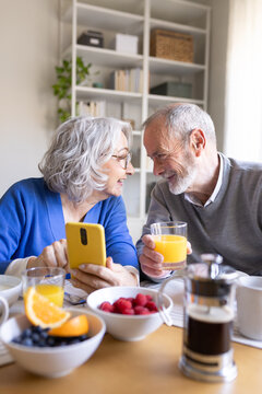 Senior couple enjoying breakfast and using smartphone at home