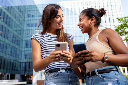 Happy young women sharing content on smartphones outdoors