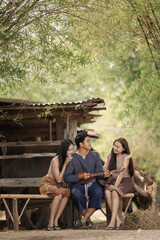Obraz premium Three Young Friends Playing Music On A Wooden Bench Outside A Traditional Bamboo Structure In A Rural Village