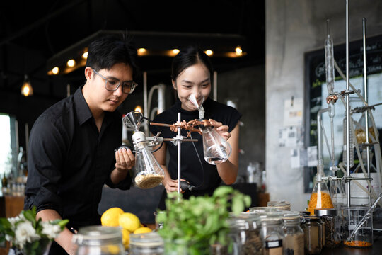Asian Perfumers Creating Fragrance in Modern Laboratory with Botanical Ingredients and Glass Distillation Equipment