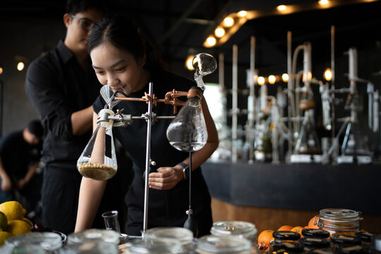 Asian Perfumers Creating Fragrance in Modern Laboratory with Botanical Ingredients and Glass Distillation Equipment