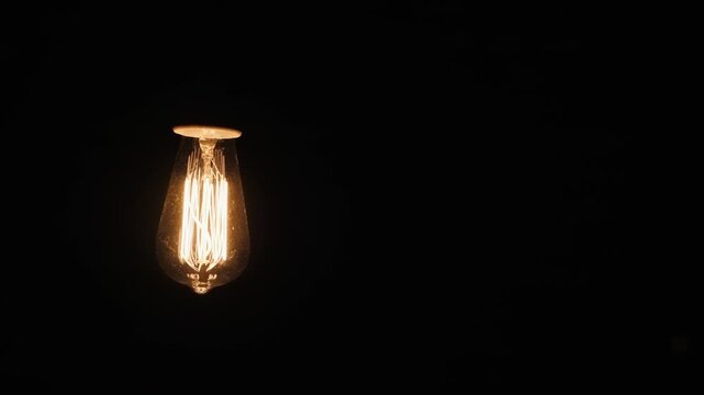 Old fashioned edison light bulb glowing in total darkness isolated on black background.