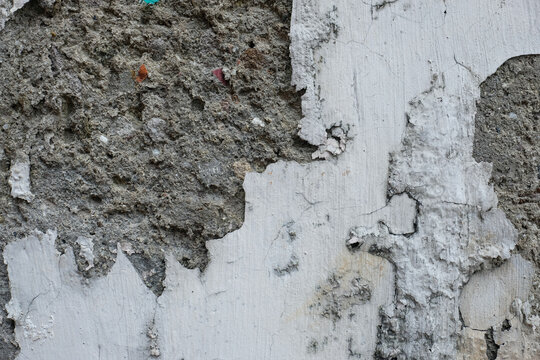Rough wall detail with thick plaster damage and peeling paint layers in gray and white tones. Suitable for construction, repair, and grunge background use.