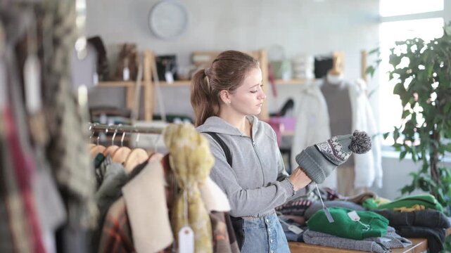  Young woman near showcase examine goods, buying hat. Off line clothing store from retailer. Style and fashion type look, modern trends. Designer clothing store, vintage fashion, limited edition