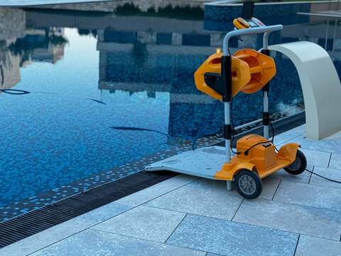 Automatic robotic swimming pool cleaner on the edge of a luxury pool with blue mosaic tiles.