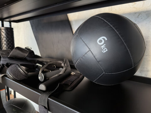 Black 6kg medicine ball on a gym shelf with functional training equipment and concrete wall.