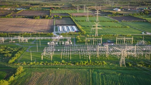 Aerial tracking shot from left to right of electrical substation with a large-scale battery energy storage system (BESS), high-voltage pylons and power lines in the background. 