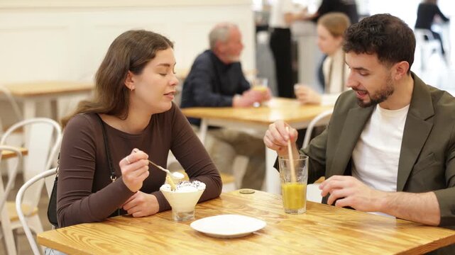 Woman and a man at a table in a cafe, they enjoys dessert and drinks. Young couple chatting in a coffee shop. High quality 4k footage