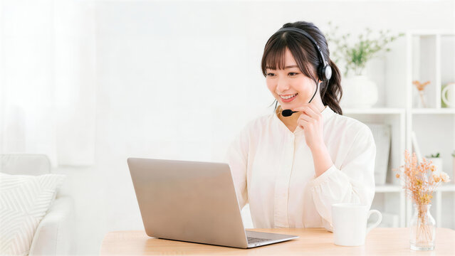 ノートパソコンを見ながら笑顔で通話するヘッドセットを付けた女性オペレーター