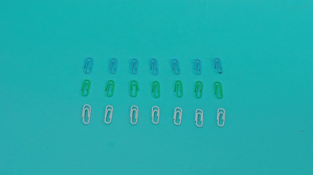 Slow Motion Video Of Flatlay Of Hand Straightening Misaligned Paper Clips On Turquoise Background