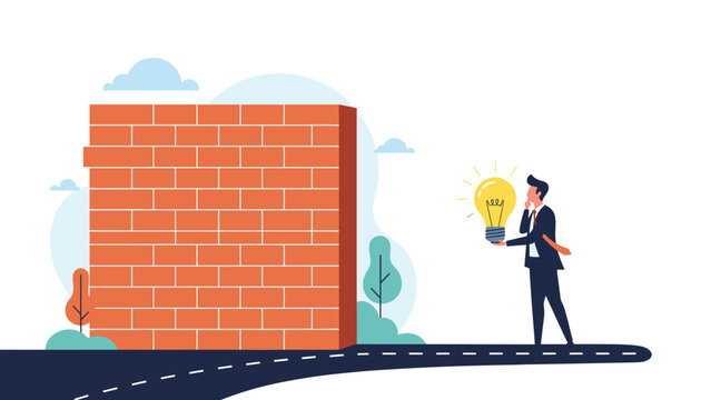 Businessman holding a glowing light bulb while standing in front of a giant brick wall blocking the road to find a creative solution.