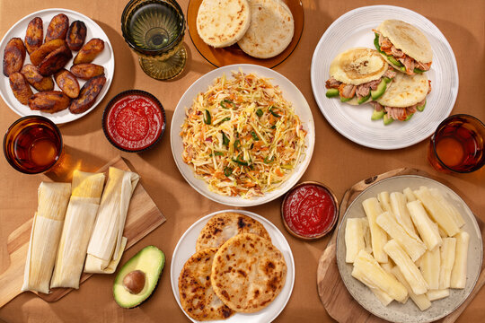 Flatlay of Latin American dishes: pupusas, arepas, curtido, tajadas, humitas, yuca
