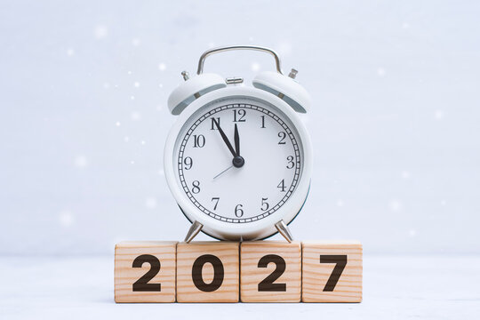 White alarm clock standing on wooden blocks with 2027 numbers represents new year countdown, deadline and future planning. Seasonal concept suitable for holiday campaigns and business goals.