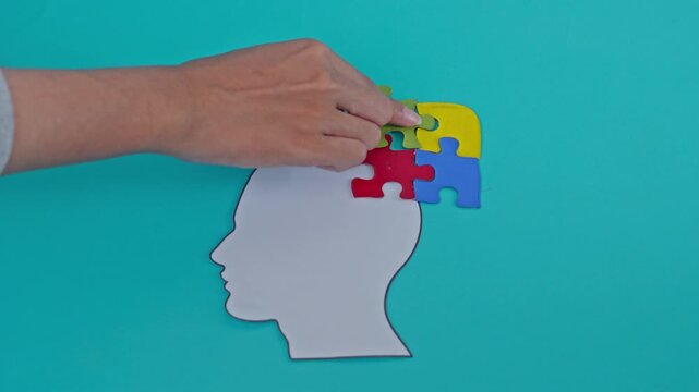 Hand Arranging Colorful Puzzle Pieces Onto Paper Head Cutout With Ocd Text On Turquoise Background