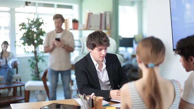 Man bank manager staff sits at desk and communicates with unrecognizable couple of clients. Manager offers options, listens to customer requests, and sells services to financial institution